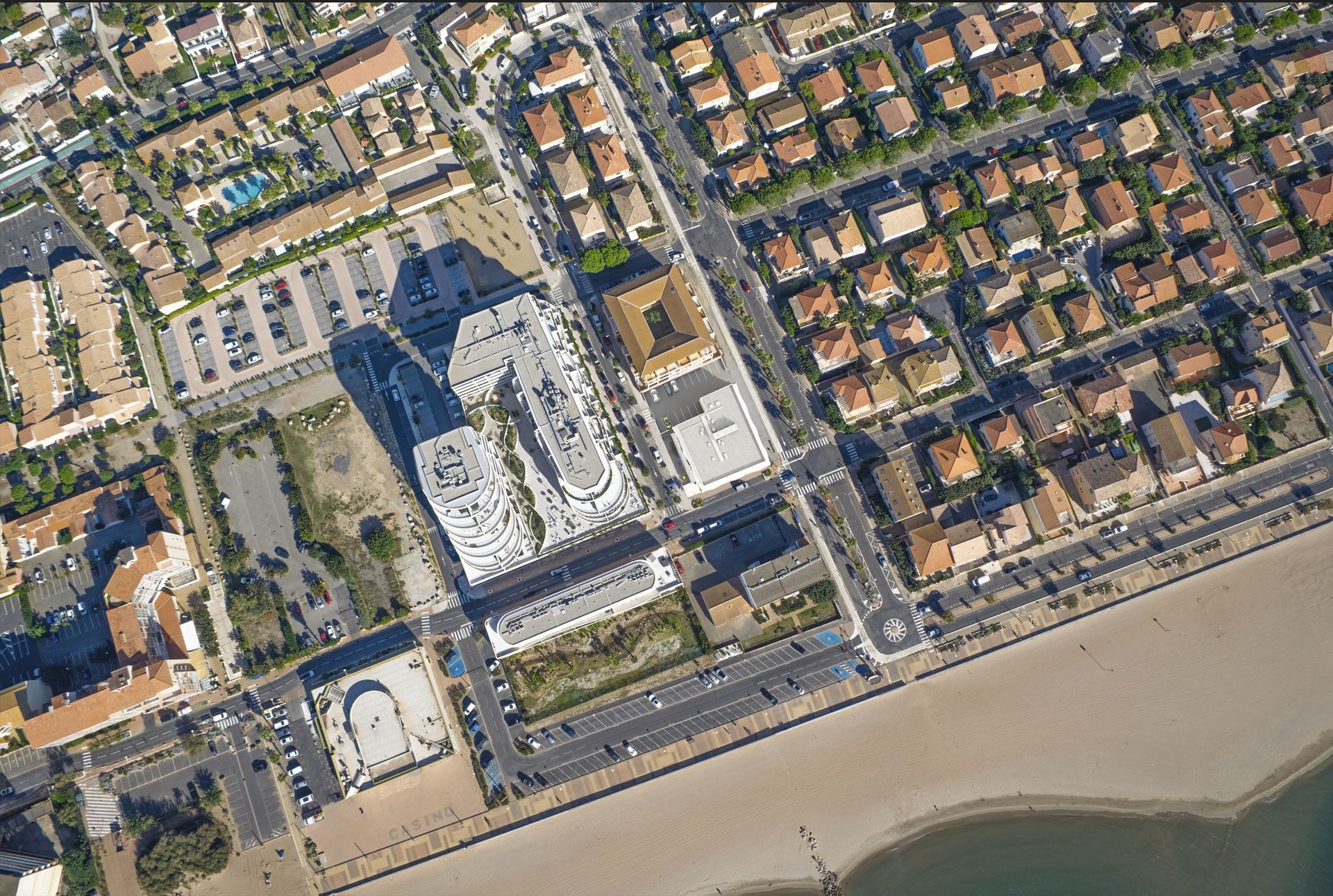 Vue aérienne d'une ville côtière avec ses bâtiments, ses routes et sa plage de sable.