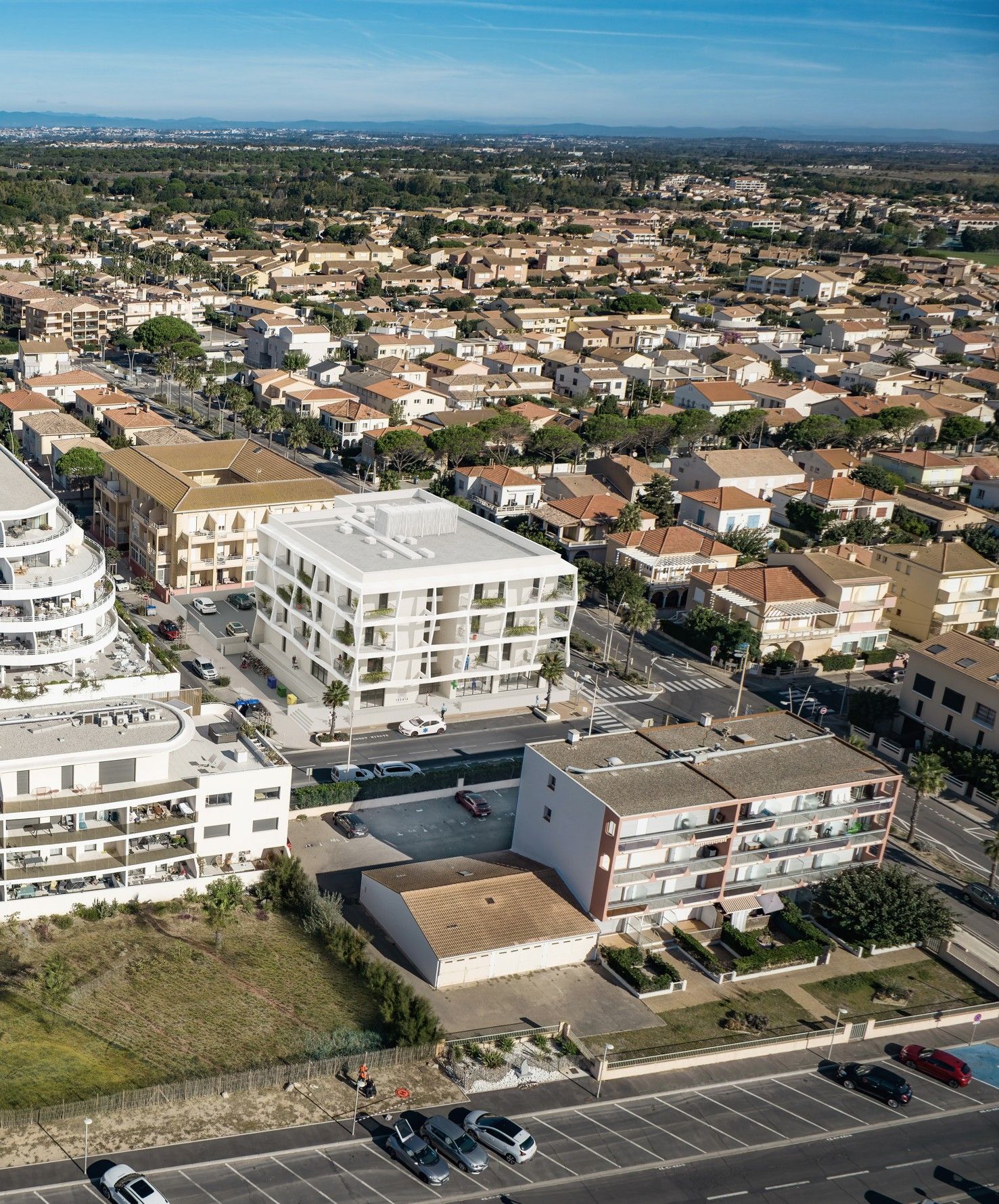 Vue aérienne d'immeubles résidentiels aux toits de tuiles rouges, près du littoral.
