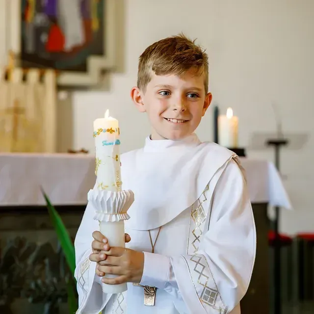 Un niño con una túnica blanca sostiene una vela en una iglesia.