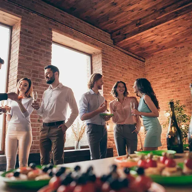Un grupo de personas están de pie alrededor de una mesa con comida y bebidas.