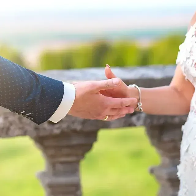 Una novia y un novio se toman de la mano delante de una barandilla de piedra.