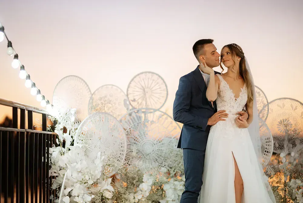 Una novia y un novio se besan delante de una valla.