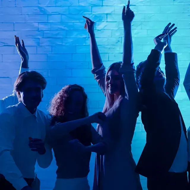 Un grupo de personas está bailando en una habitación oscura con los brazos en el aire.