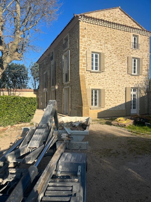 Camion déposant une benne à gravats de 3m3 dans la cour d'une belle maison en pierre en cours de rén