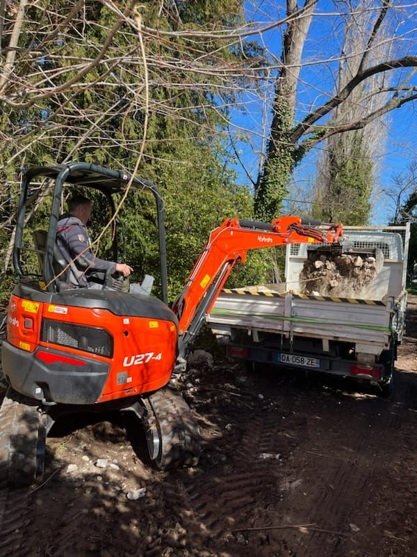 Une personne conduit une mini-pelle et charge du bois dans une benne