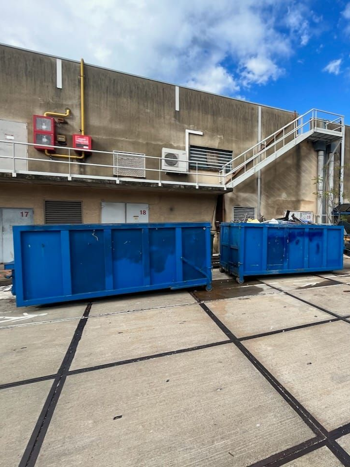 Deux bennes bleues se trouvent devant un bâtiment