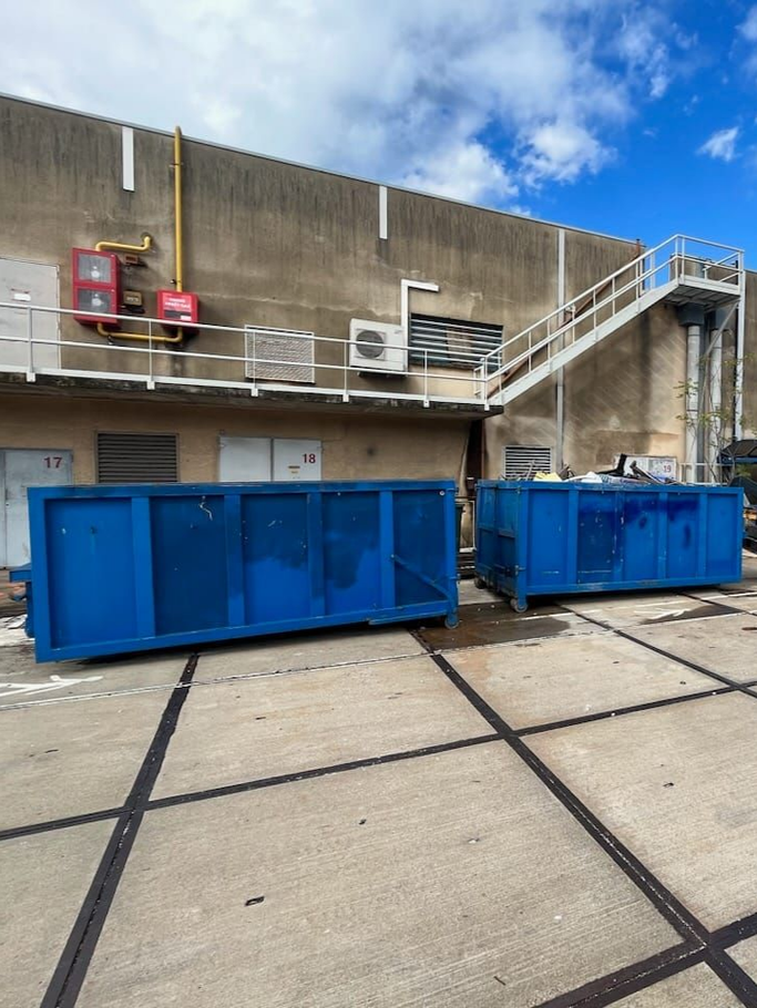 Deux bennes bleues se trouvent devant un bâtiment