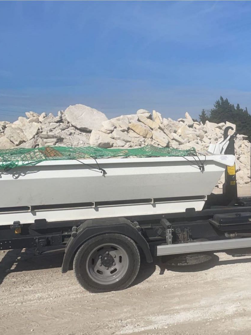 Un plateau de camion blanc rempli de pierres avec un tas de pierres en arrière-plan