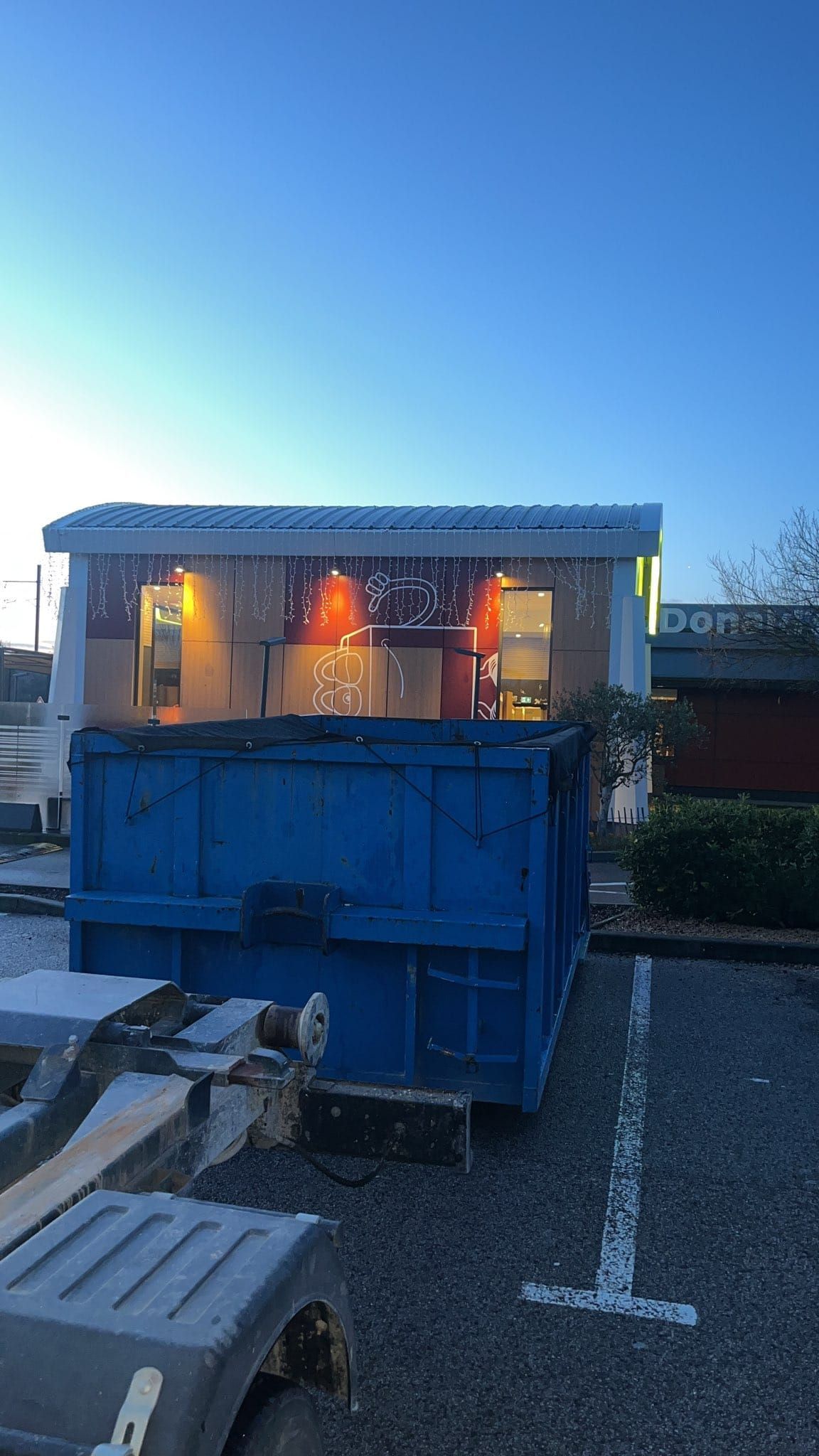 Camion ampliroll déposant une benne bleue sur le parking du restaurant McDonald's à Bagnols-sur-Cèze