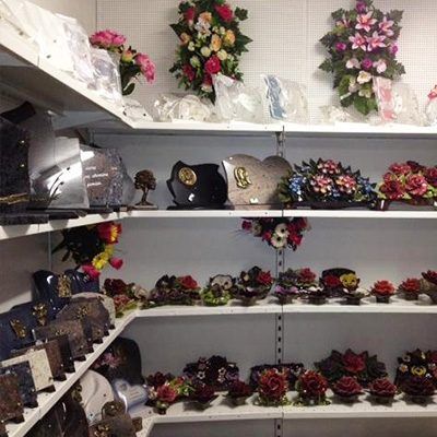 Des étagères présentent des articles commémoratifs : pierres tombales, compositions florales et vases.