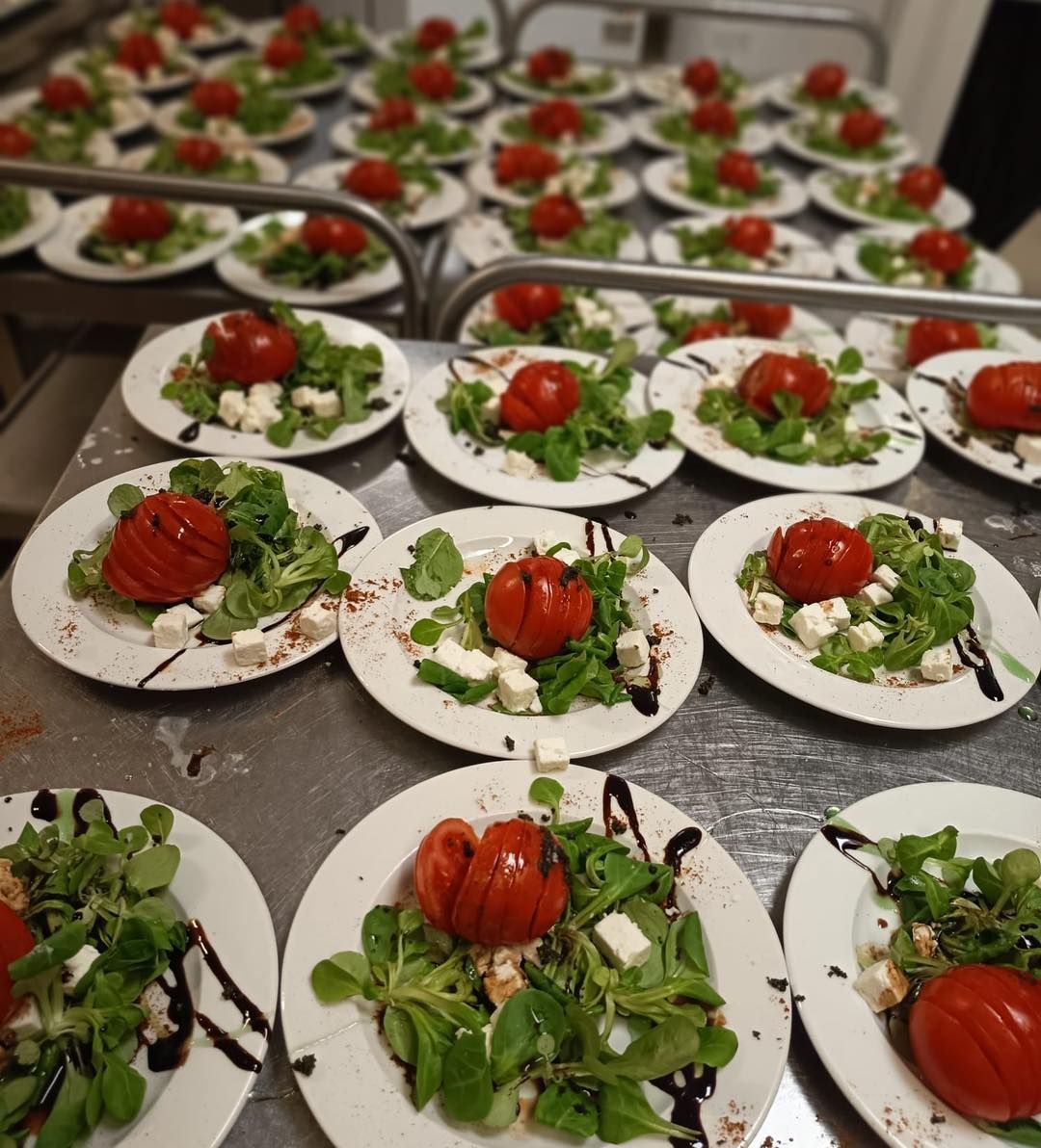 Plusieurs assiettes de salade fraîche avec un glaçage balsamique, du fromage en dés et une tomate rôtie entière.