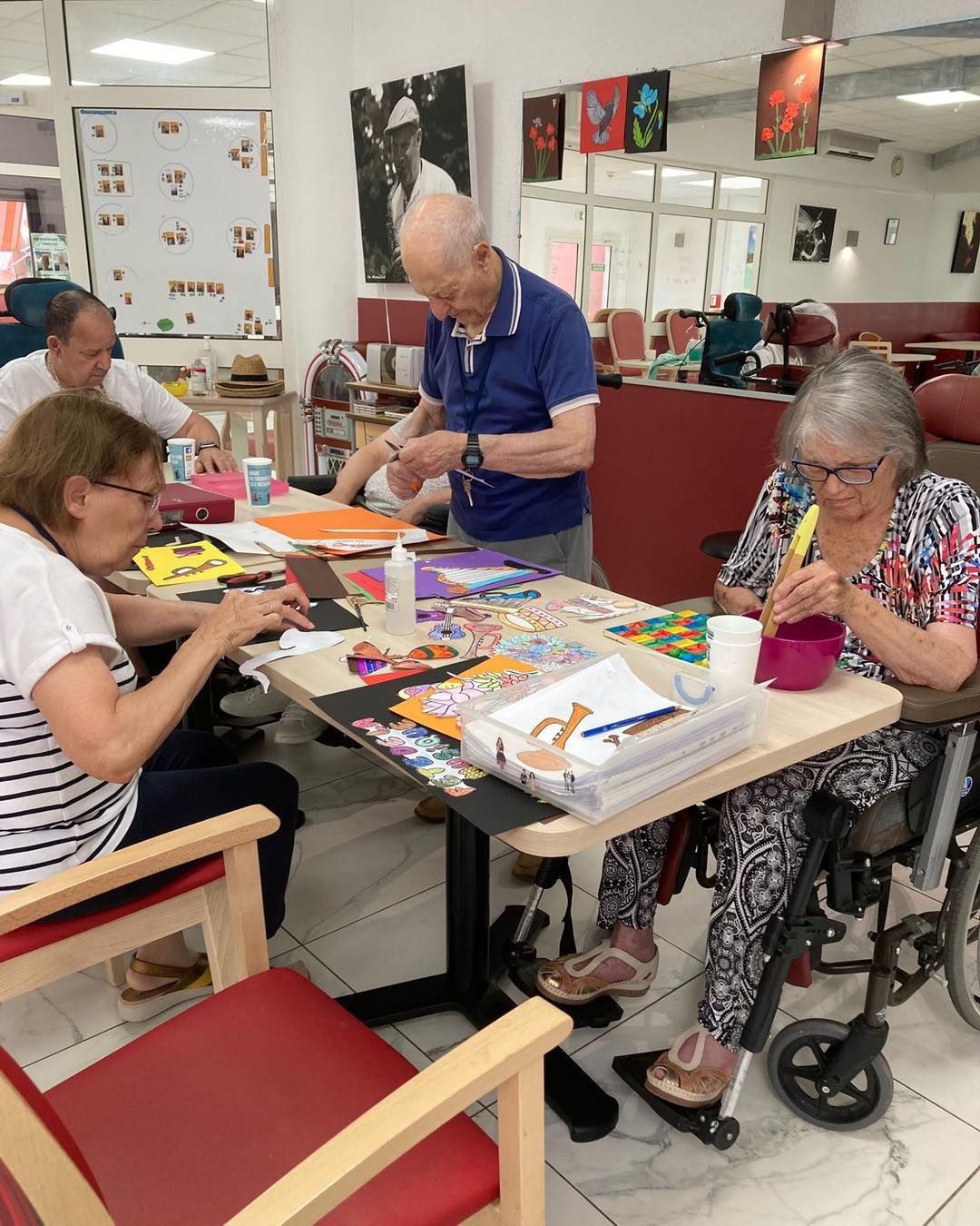 Des personnes bricolent autour d'une table dans une salle communautaire lumineuse, avec du matériel d'art et de couture.
