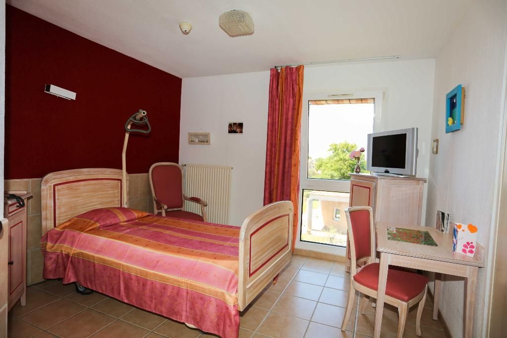 Une chambre en EHPAD avec un lit, une télévision, un bureau et une fenêtre.