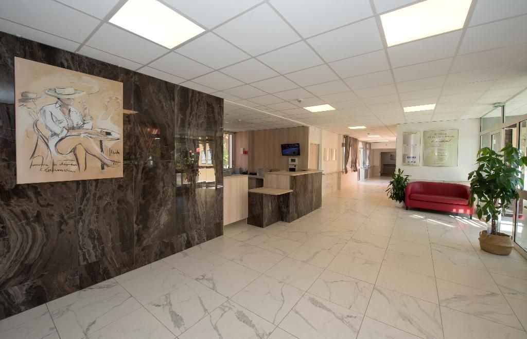 Hall d'entrée moderne avec sol carrelé blanc, comptoir d'accueil en marbre, œuvres d'art abstraites aux murs et canapé rouge.
