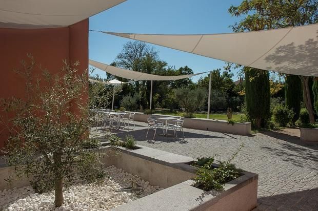 Une terrasse extérieure avec des tables et des chaises blanches, ombragée par des voiles.