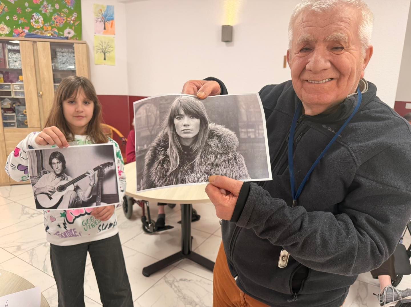 Un homme âgé et une jeune fille tiennent des portraits en noir et blanc.