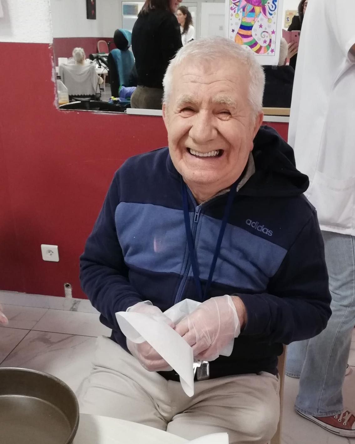 Une personne souriante, vêtue d'une veste bleu marine et de gants, est assise à l'intérieur, tenant du papier cuisson.