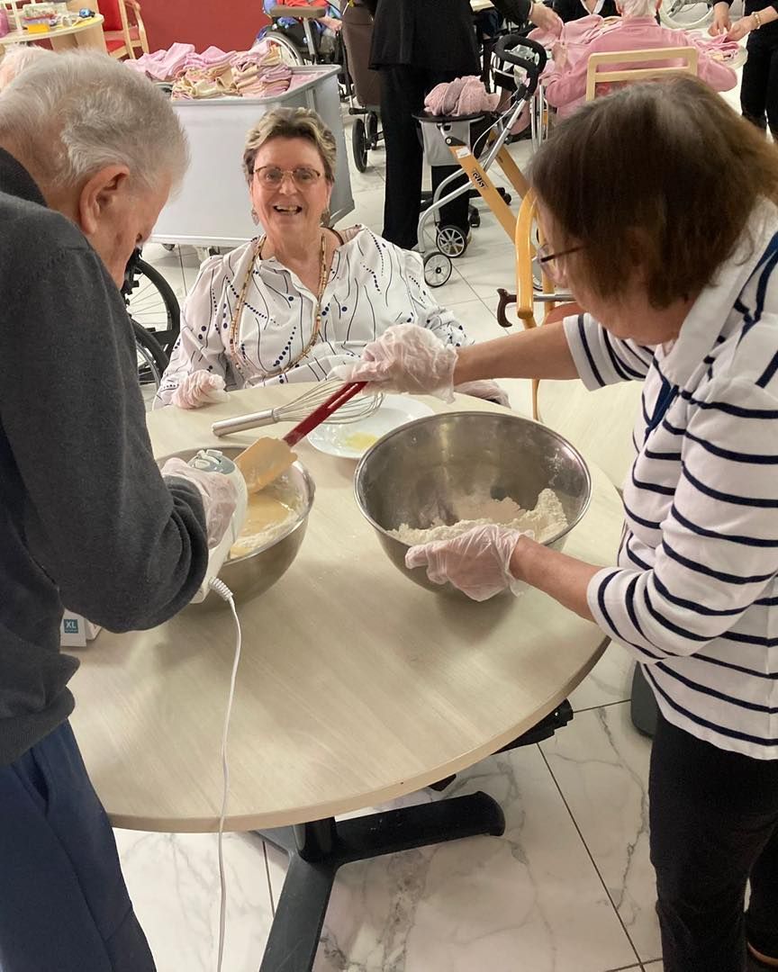 Dans une cuisine communautaire lumineuse, trois personnes préparent une pâte à pâte autour d'une table ronde.