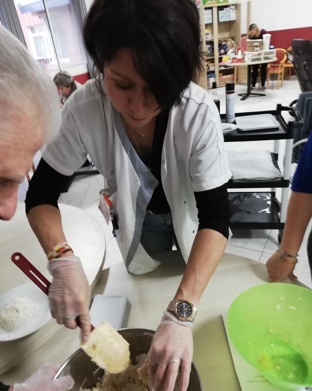Des personnes préparent le repas à table, l'une d'elles versant les ingrédients dans un bol à la cuillère.