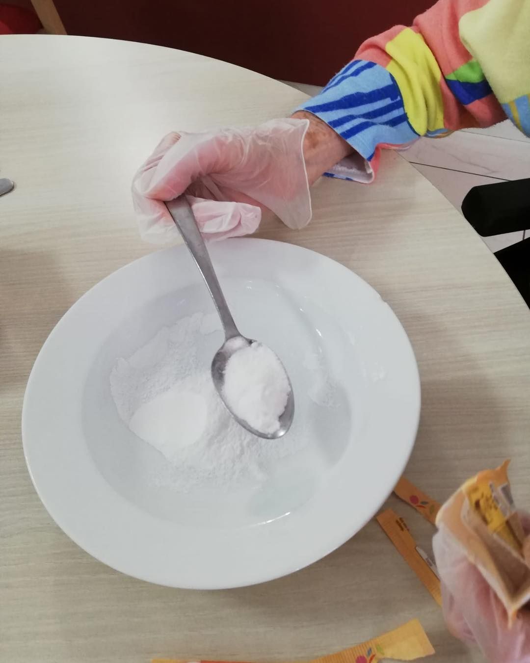 Main gantée tenant une cuillère au-dessus d'une assiette blanche sur laquelle repose un monticule de poudre blanche.