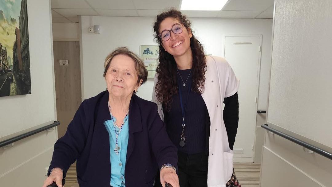 Une kinésithérapeute accompagne une personne âgée en désambulateur.