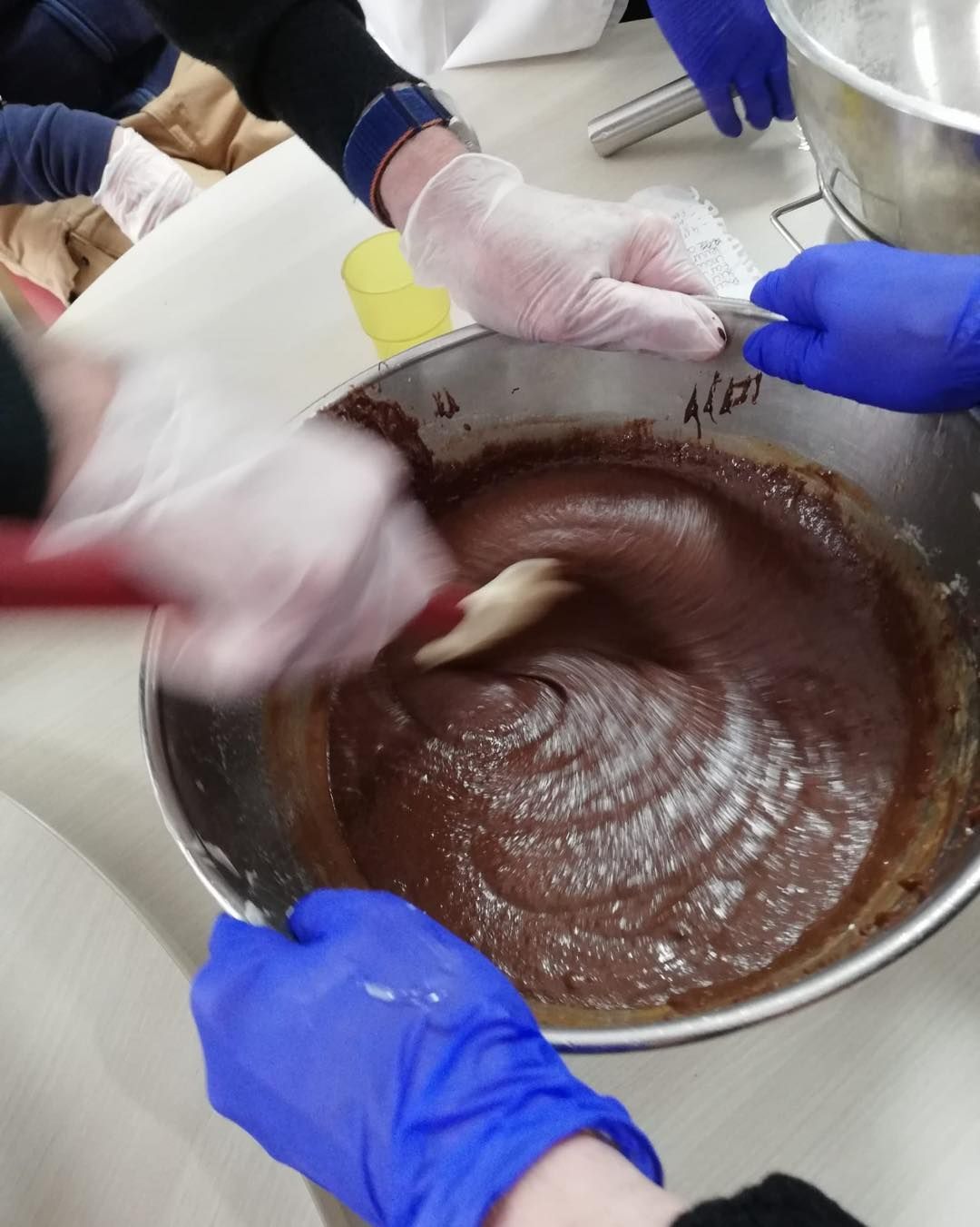 Des mains gantées remuent un grand bol de pâte brune épaisse à l'aide d'une spatule.