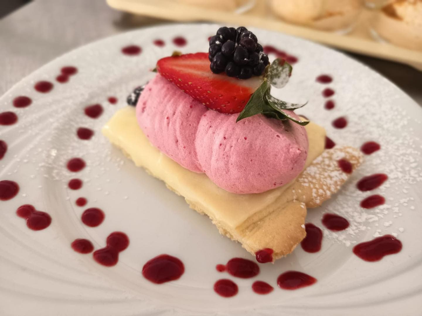 Assiette de dessert composée de mousse rose, de fraises et de mûres, nappée de coulis de fruits rouges