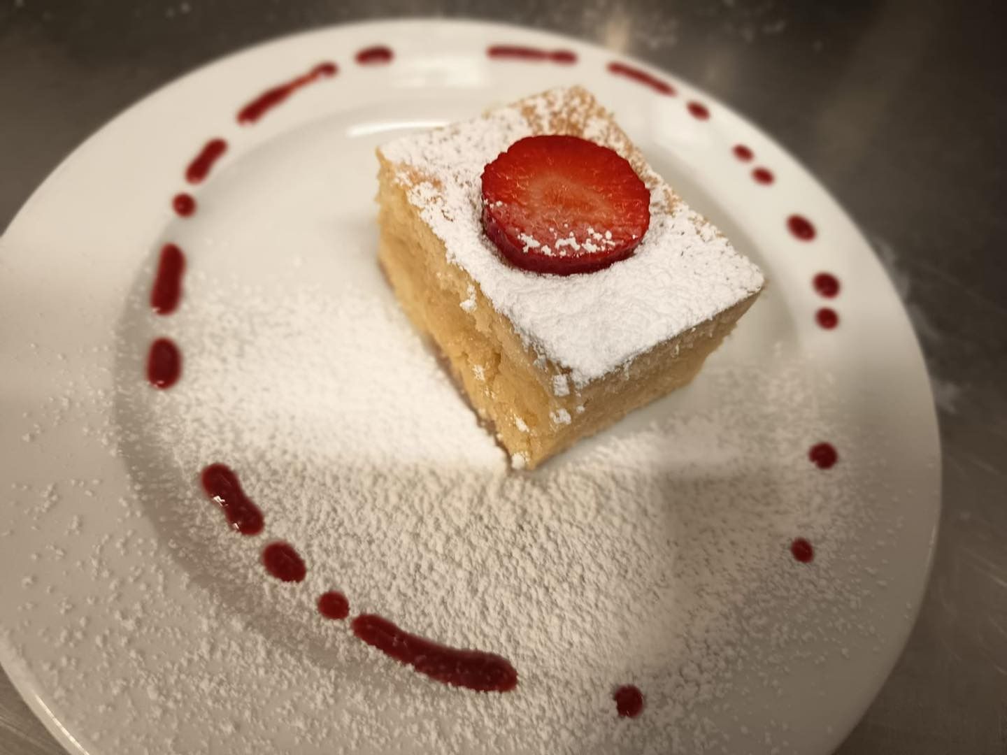 Carré de dessert en poudre avec une tranche de fraise sur une assiette blanche, arrosé de sauce tomate