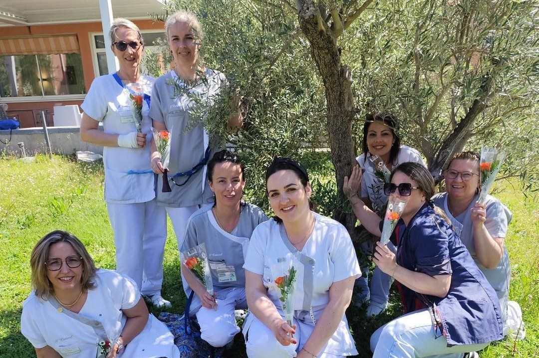 Personnel d'EHPAD en uniforme blanc posant à l'extérieur sur la pelouse, avec des arbres en arrière-plan.