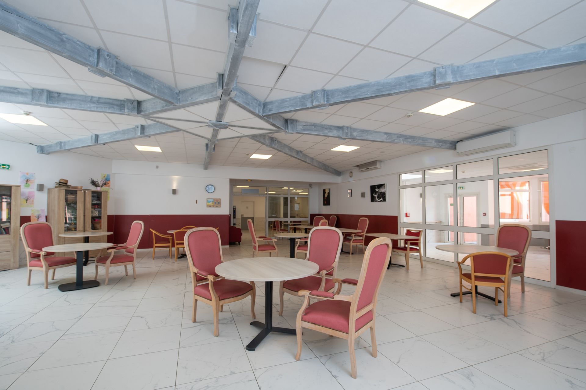 Une salle à manger spacieuse avec plusieurs tables rondes et des chaises rouges.