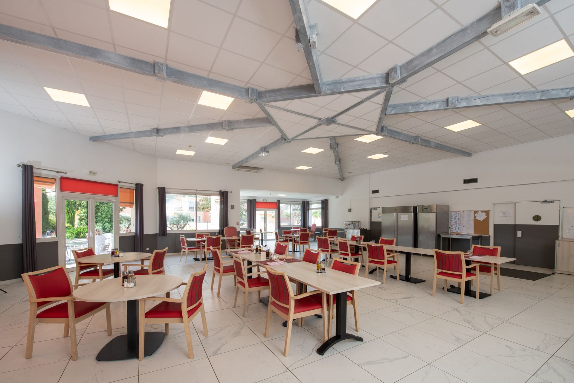 Une salle à manger ouverte avec plusieurs tables carrées et des chaises rouges.