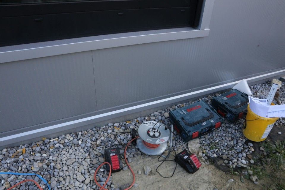 Werkzeuge und Kabel in der Nähe der grauen Fassade eines Gebäudes und eines Kiesbetts.