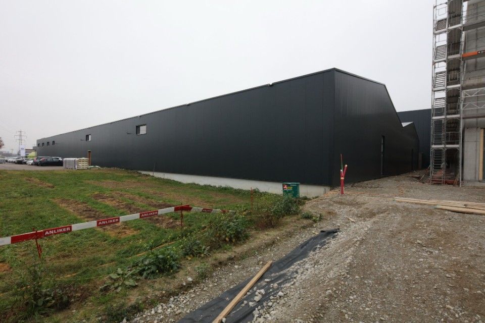 Schwarzes Industriegebäude unter bewölktem Himmel. Baumaterialien und Schmutz im Vordergrund.