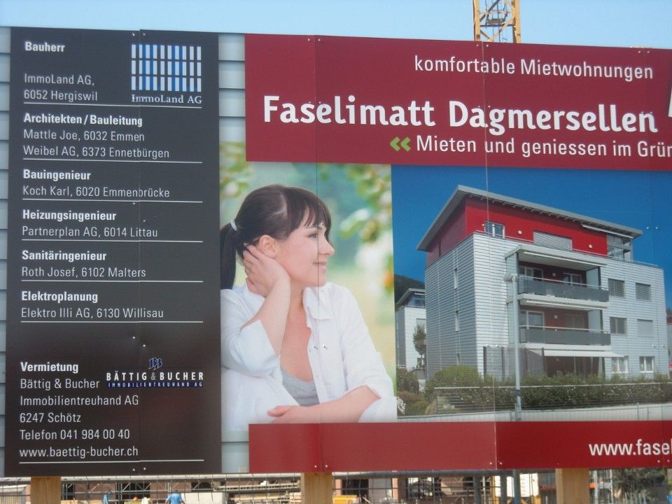 Baustellenschild: Werbung für ein Gebäude mit einer Frau, einem modernen Gebäude und einem Text über Wohnungen in Dagmersellen, Schweiz.