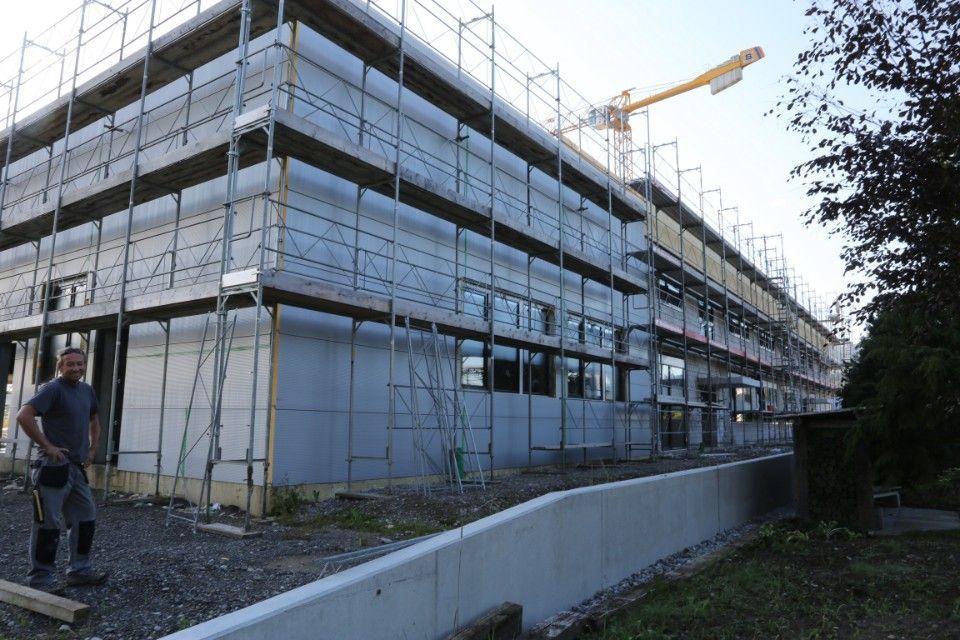 Bau eines mehrstöckigen Gebäudes mit Gerüst. Ein Arbeiter steht davor. Ein Kran ist zu sehen.