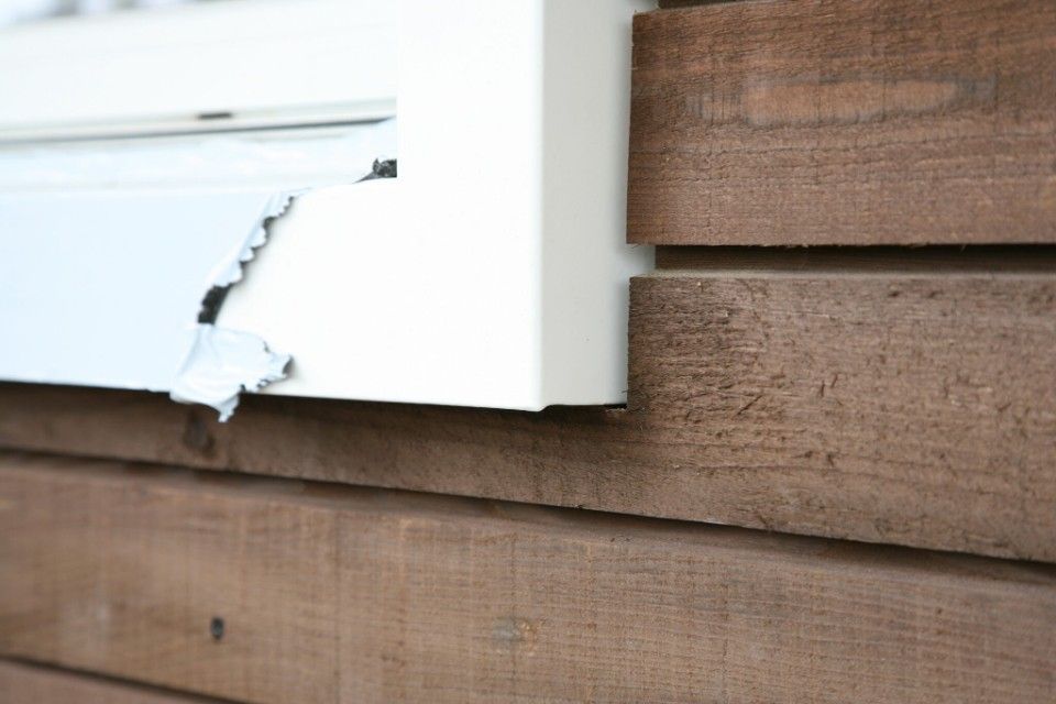 Beschädigte weisse Zierleisten an einer holzgetäfelten Wand. Abgeplatzte Farbe gibt eine blaue Schicht frei.