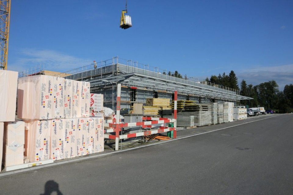 Baustelle mit Kran, Baumaterialien und einem teilweise errichteten Bauwerk unter blauem Himmel.