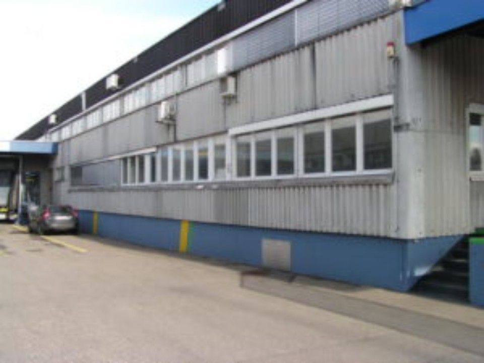 Aussenansicht eines Geschäftsgebäudes mit Wellblechverkleidung, Fenstern und blauen und gelben Akzenten.