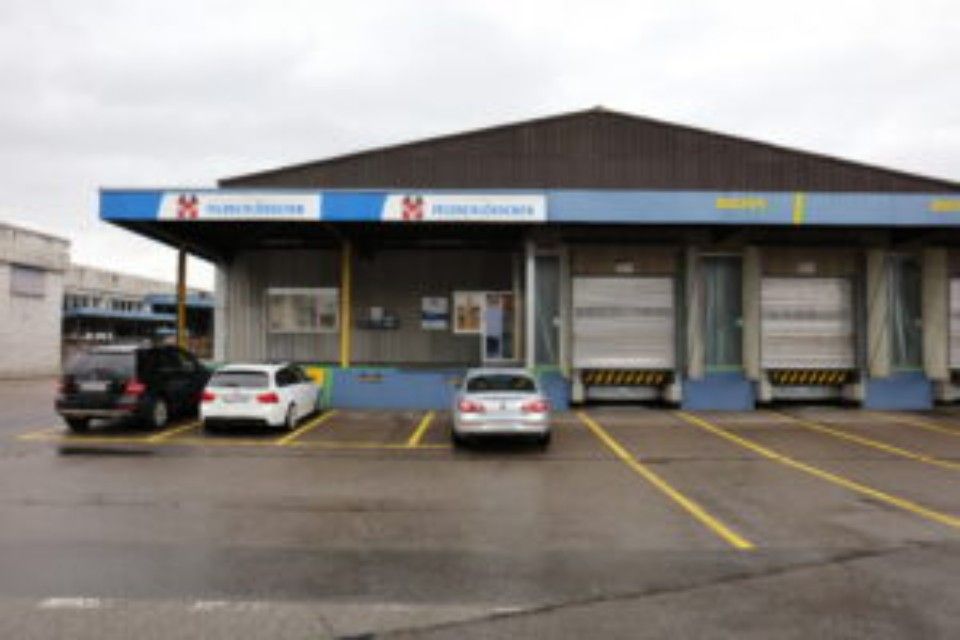 Aussenansicht eines Gebäudes mit Laderampen, davor geparkten Autos und einem blau-weissen Schild mit der Aufschrift „Stöcklin“.