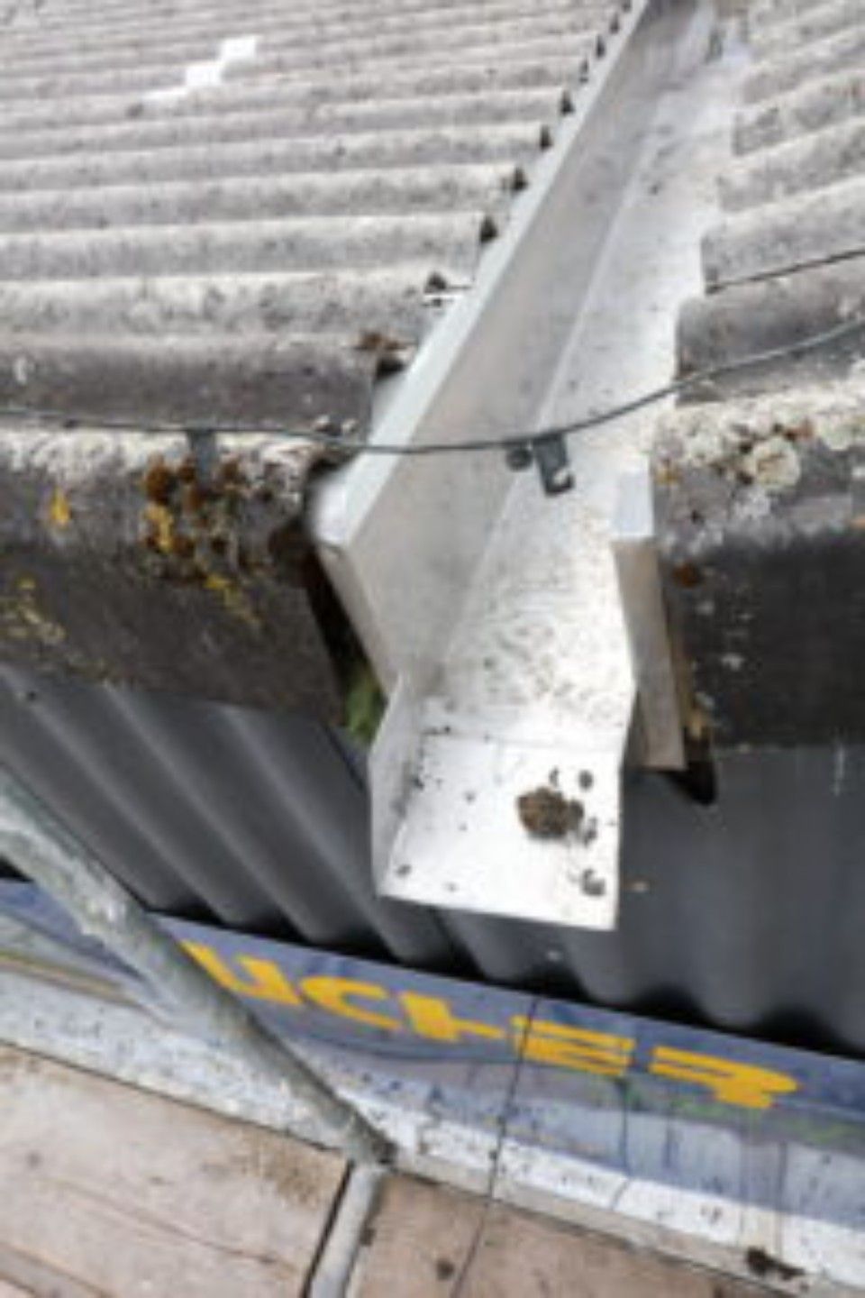 Beschädigte Metallrinne auf einem Wellblechdach. Moos und Schmutz sind vorhanden.