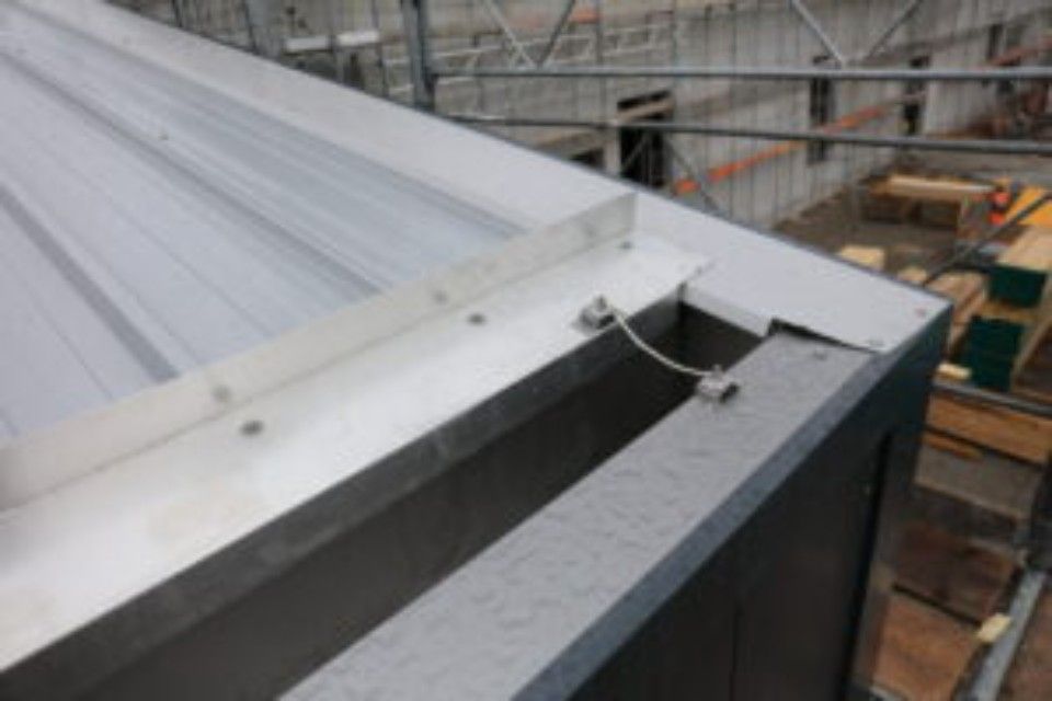 Montage von Metalldachkanten mit Dachrinne und Sicherheitskabeln auf einer Baustelle.