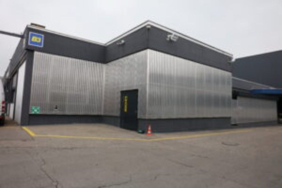 Aussenansicht eines Geschäftsgebäudes mit Wellblechverkleidung, dunkelgrauen Zierelementen und einer schwarzen Tür.