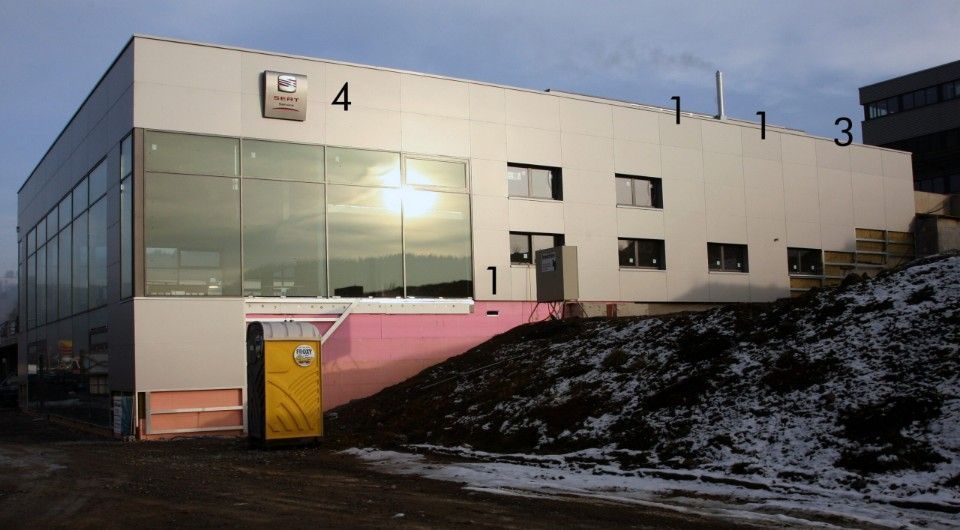 Aussenansicht eines modernen Gebäudes mit grossen Fenstern, mehreren Schornsteinen und einer Baustelle.