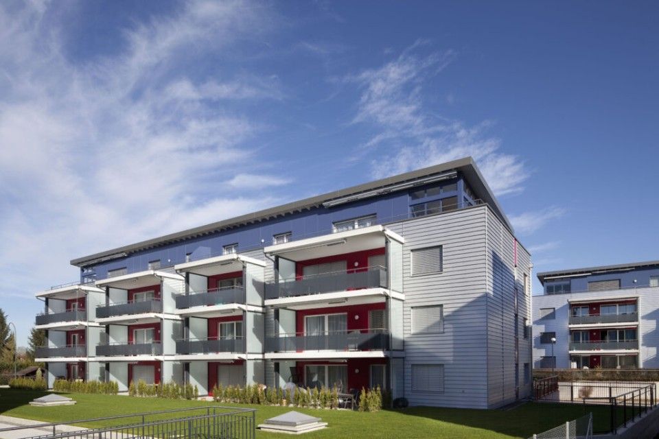 Modernes Wohnhaus mit roten Balkonen und blauem Himmel.