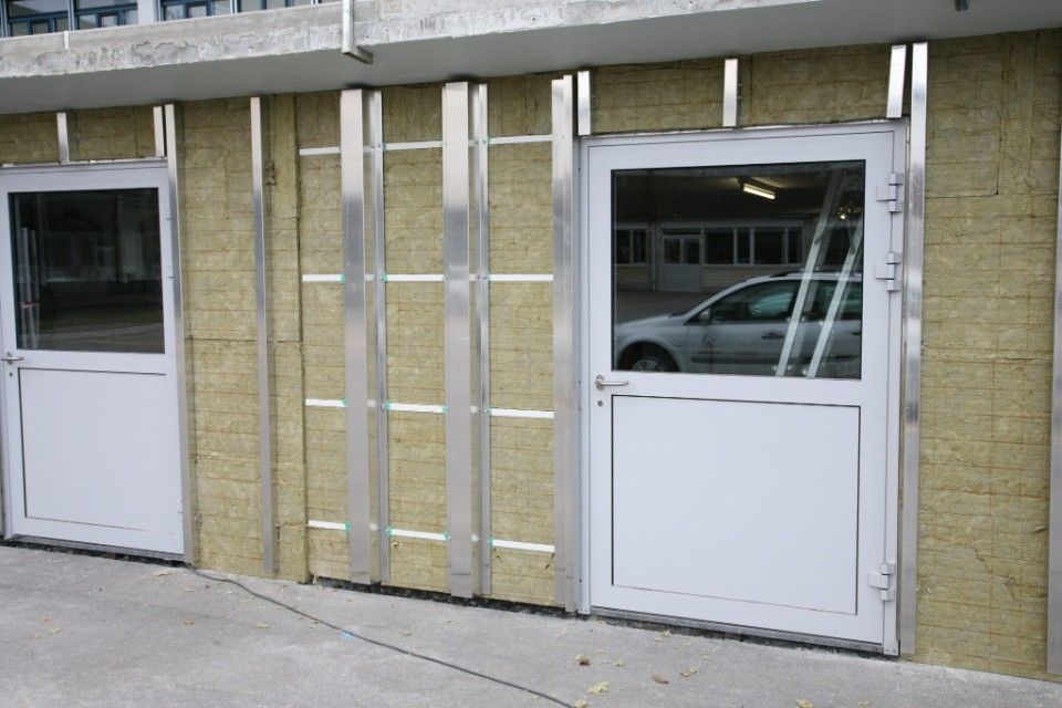 Zwei weisse Türen mit Glasscheiben, die in eine im Bau befindliche Wand eingelassen sind; vertikale Metallständer mit Isolierung.