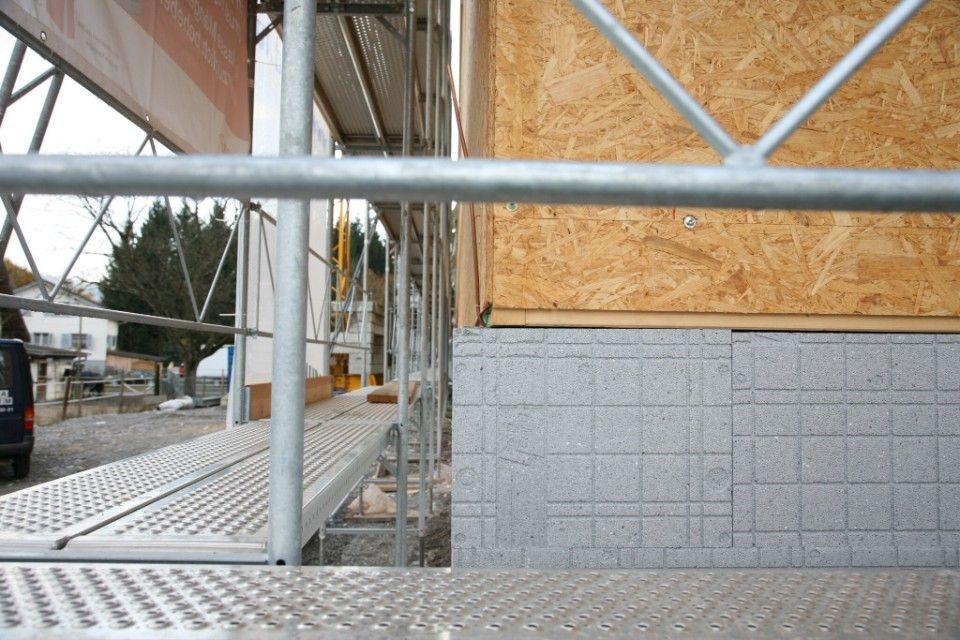 Baugerüst neben einem im Bau befindlichen Gebäude, Holzpaneele und graue Dämmung sind sichtbar.
