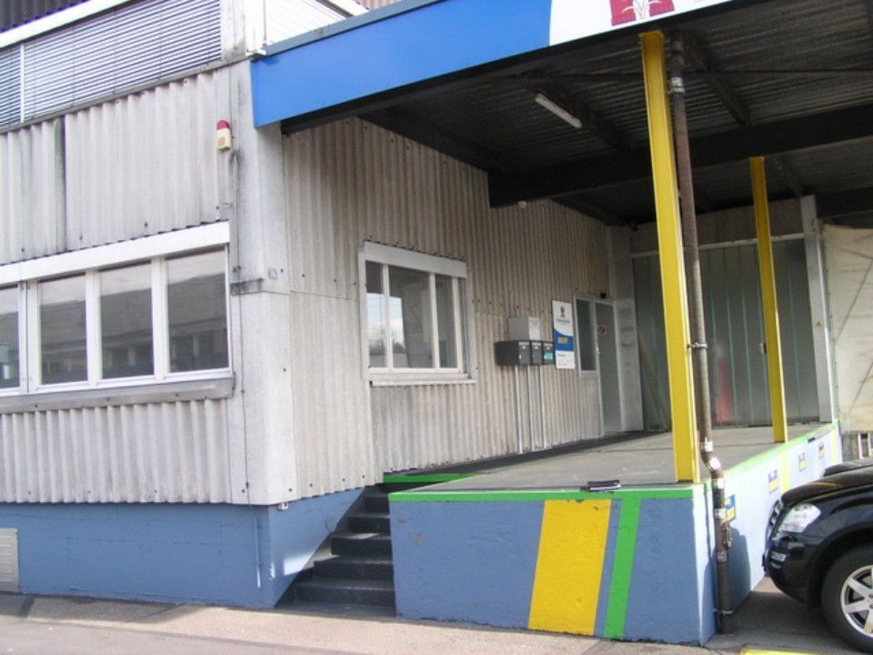 Laderampe eines Wellblechgebäudes mit blauen und gelben Akzenten. Stufen führen zu einem erhöhten Eingang.