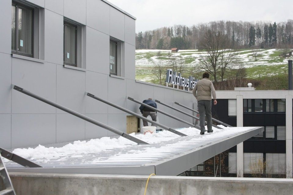 Männer auf einem Hausdach mit Schnee, schrägen Stützbalken und einem Schild.