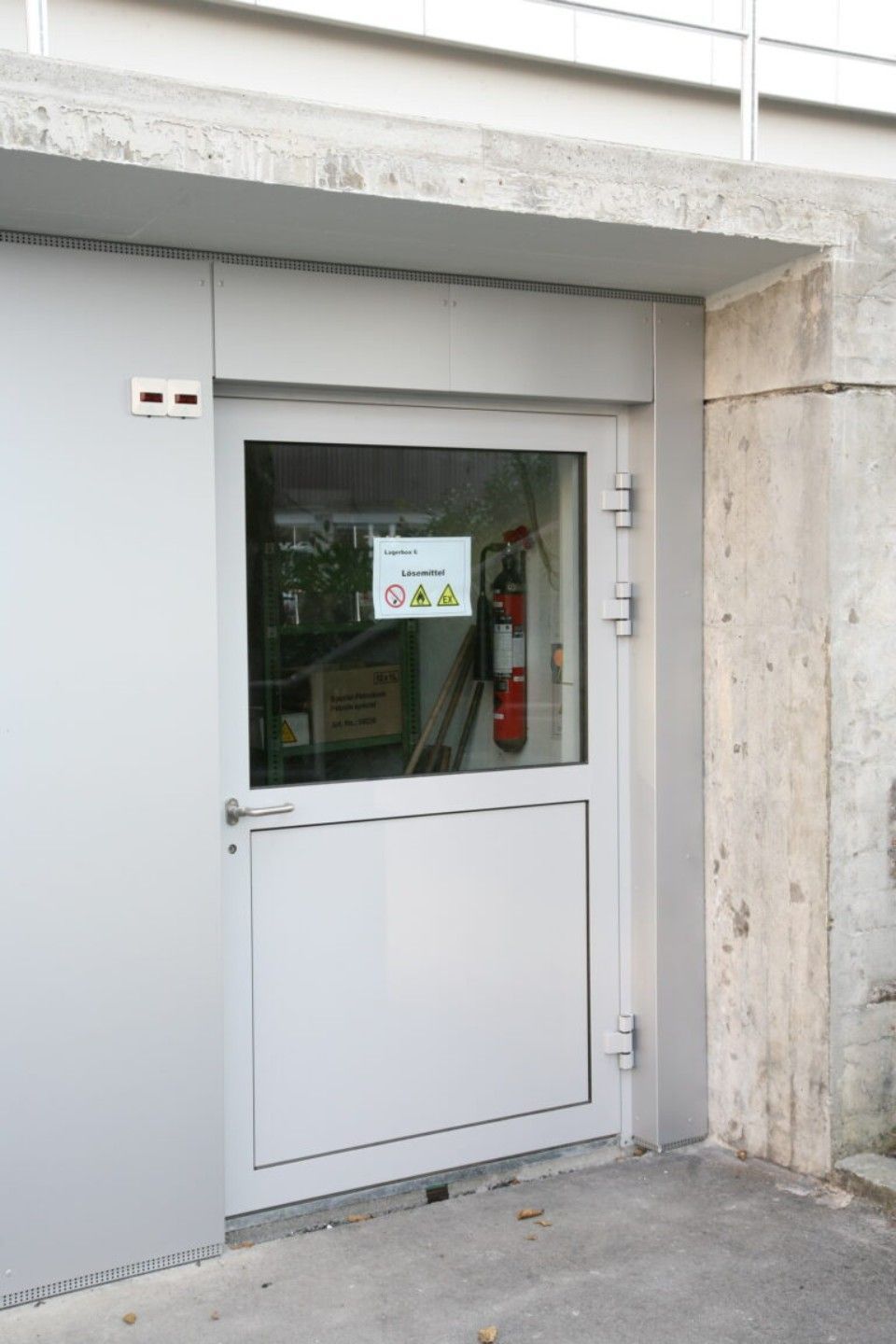 Weisse Tür mit Fenster und Sicherheitsschildern, möglicherweise der Eingang zu einem Hauswirtschaftsraum.