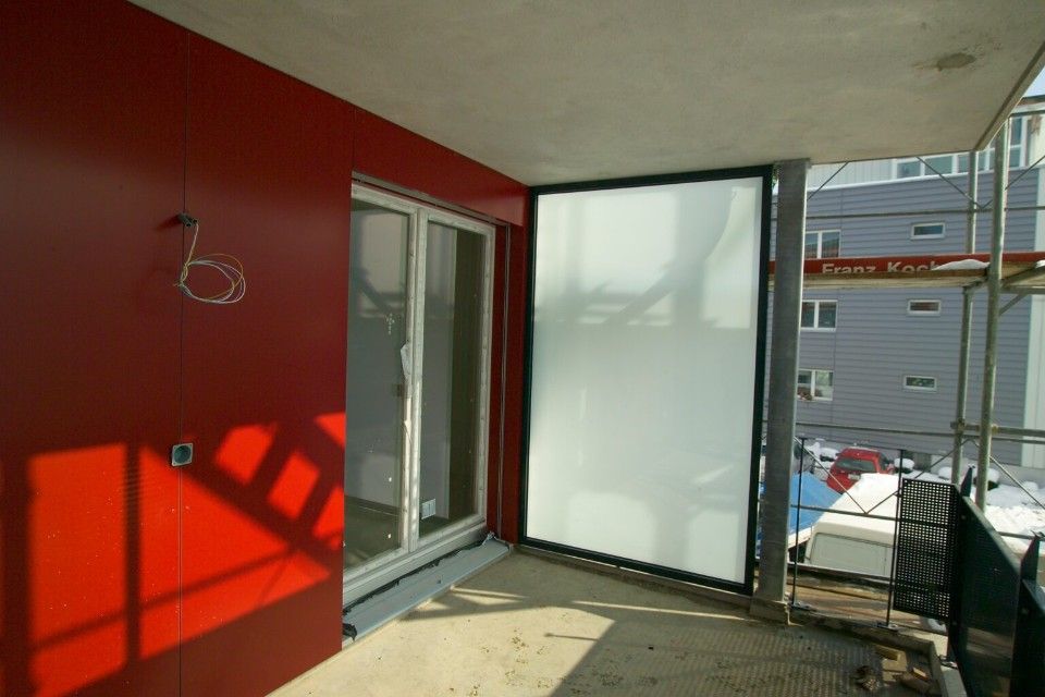 Rote Wand und Milchglas-Schiebetür auf einem im Bau befindlichen Balkon.